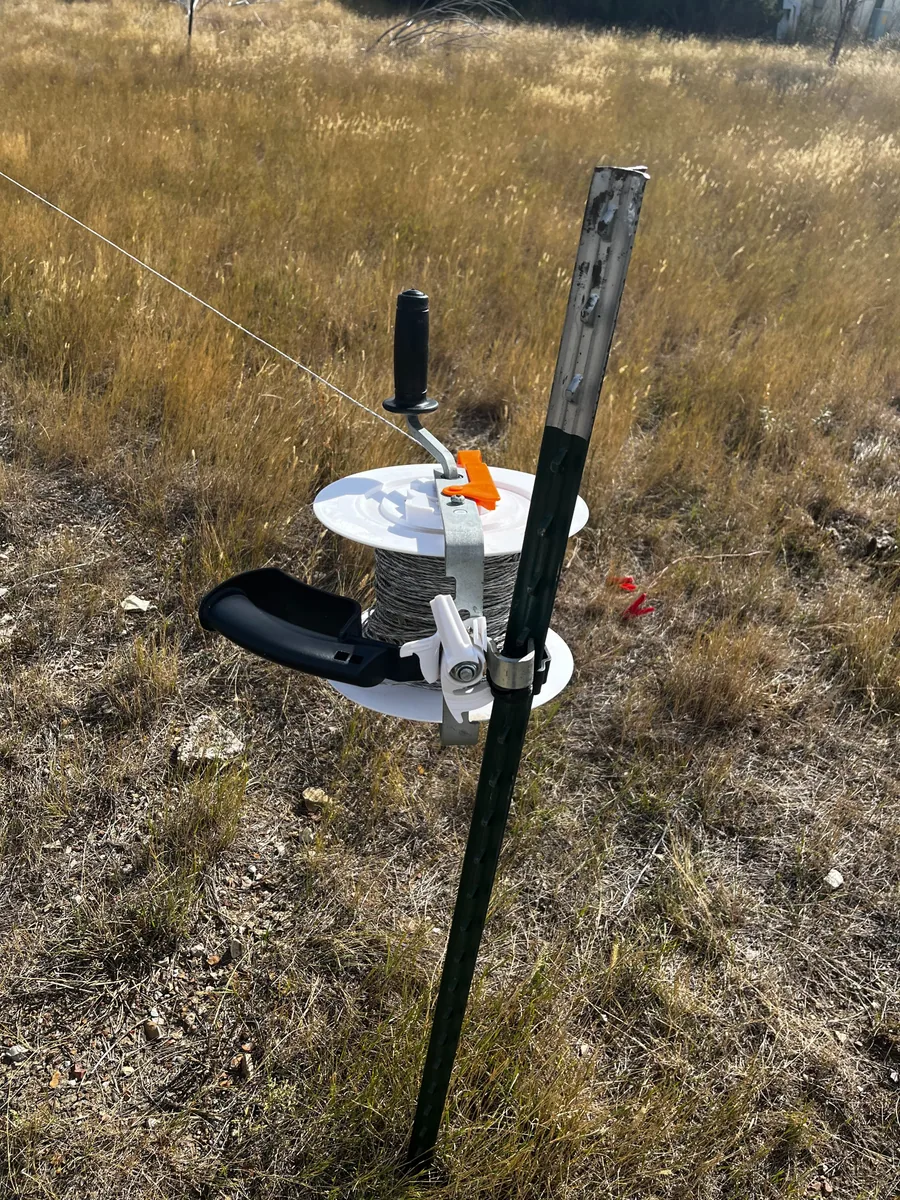 Electric fence reel with orange and white replacement parts in evening field light
